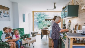 Una familia en una sala de estar con un sofá verde, una mesa de comedor y una zona de cocina con estufa.