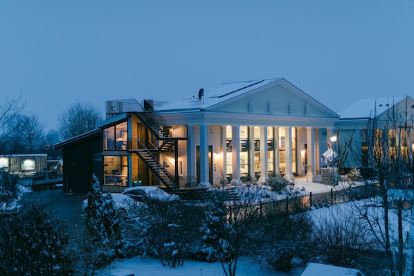 Ein modernes Haus mit großer Glasfassade, einer überdachten Veranda und verschneiter Landschaft.