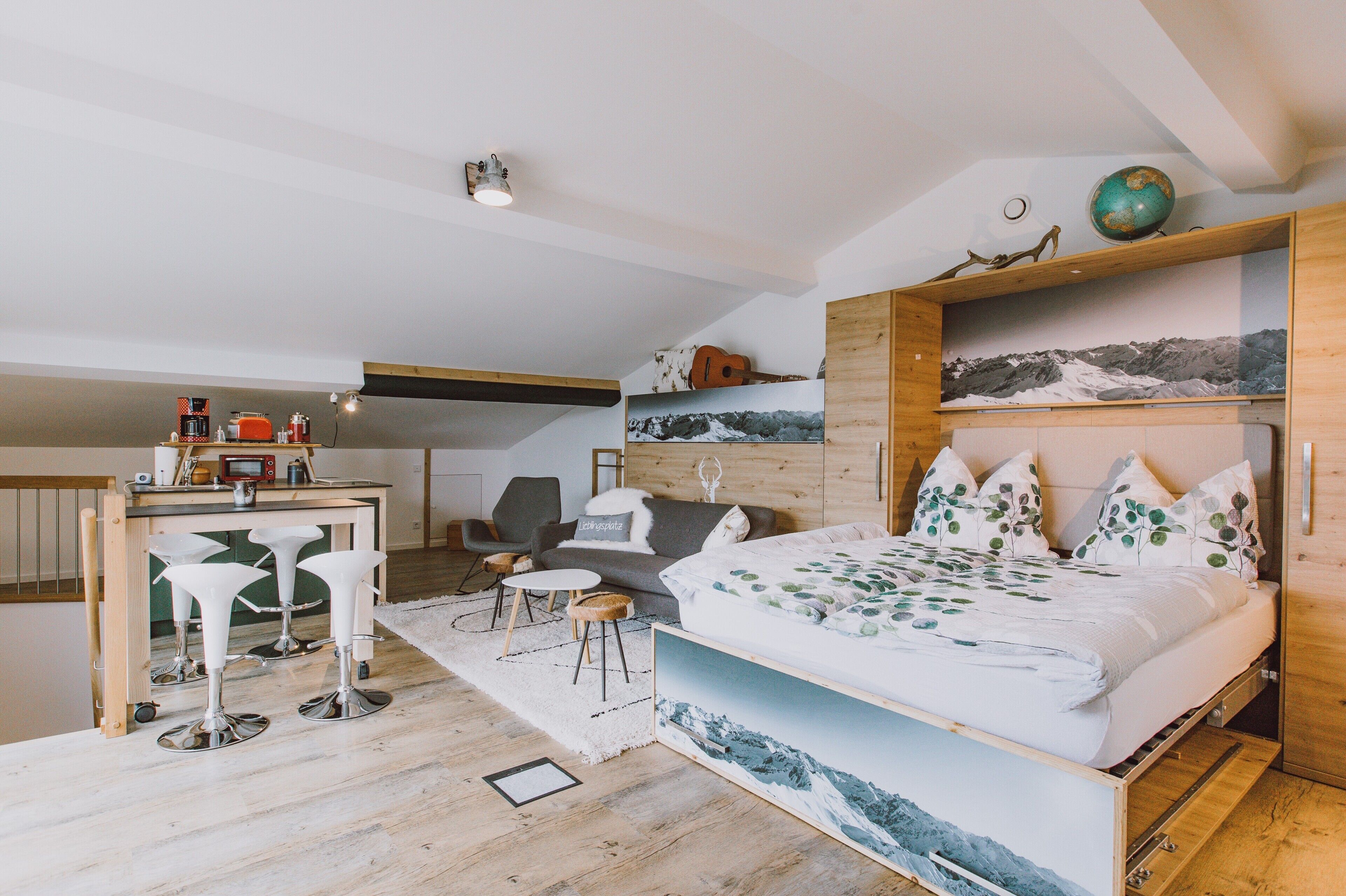 A bedroom with a bed, a desk, bar stools, a chair, and a small table.