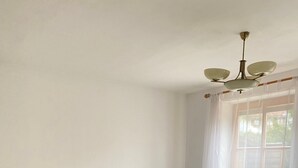 Yhden hengen sänky, jossa on puinen pääty ja jalkopää, yöpöytä, jossa on yksi laatikko, ja ikkuna, jossa on ohuet verhot.