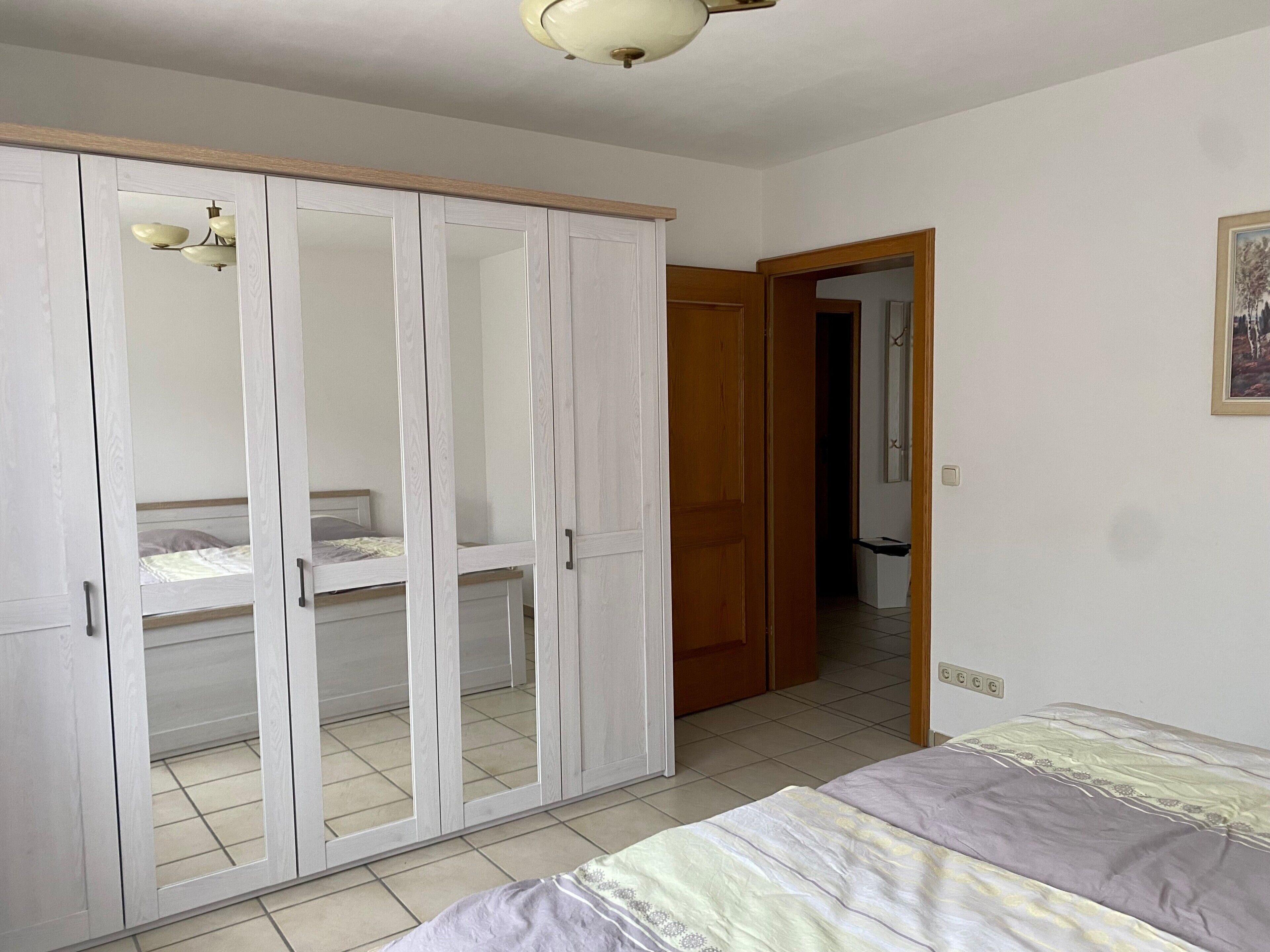 A bedroom with a bed, a wardrobe, and a door leading to another room.