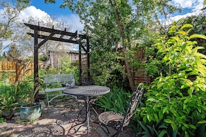 Ein Garten mit einer Terrassenüberdachung, einem Metalltisch und Stühlen.