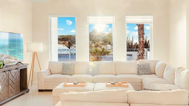 A spacious living room with a large sectional sofa, a flat-screen TV, and a view of the ocean through large windows.
