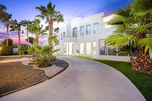 Un edificio moderno con una entrada curva bordeada de palmeras y un césped cuidado.