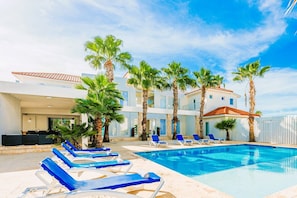 A pool area with lounge chairs and palm trees. - Beachfront 7BR Villa | Private Pool | Sleeps 16+ - Blue Door Beach House (Noord)