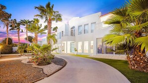 A modern building with a curved driveway, surrounded by palm trees and a well-maintained lawn.