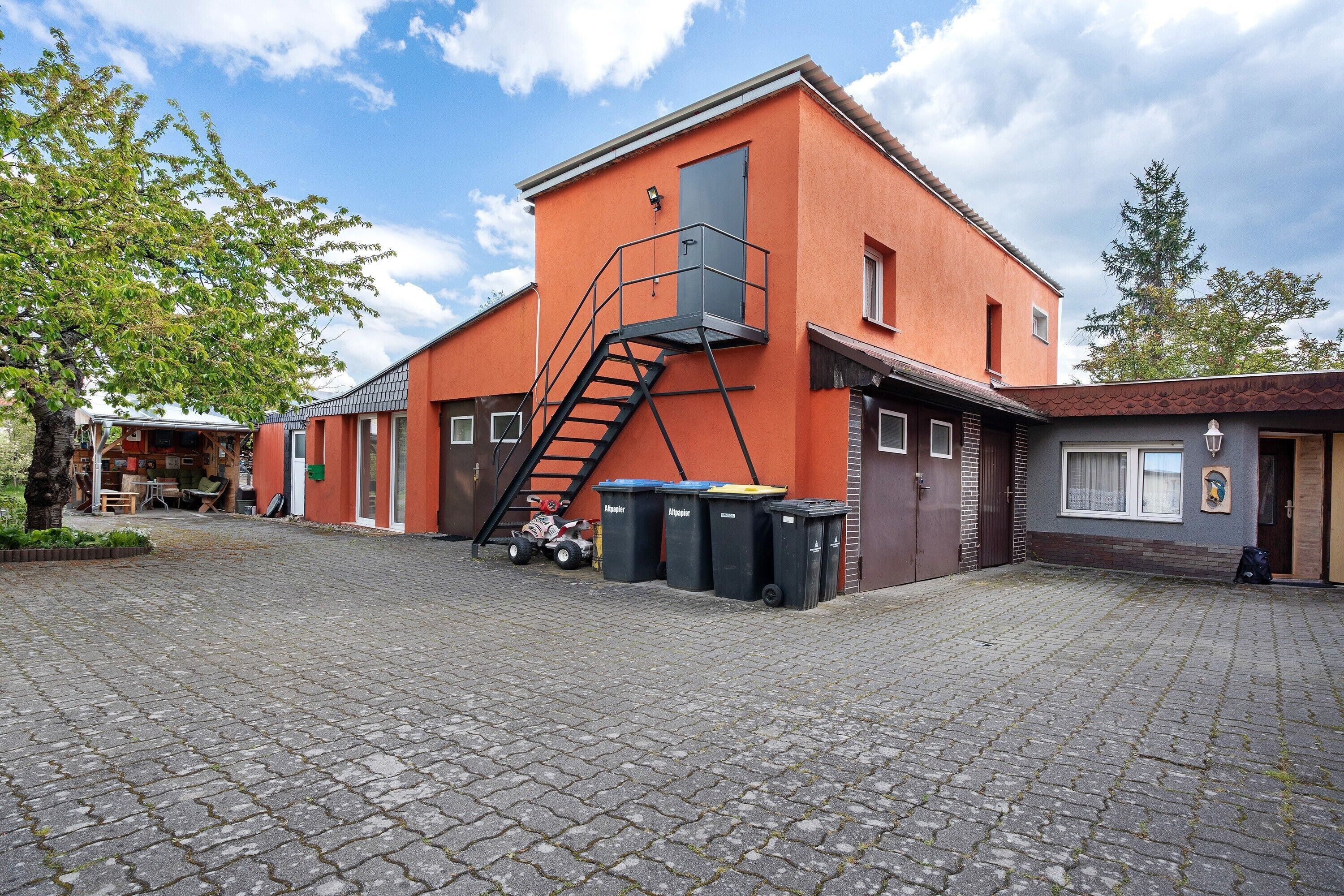 Ein Gebäude mit roter Fassade, einer Treppe, die zu einem Balkon führt, und mehreren Mülltonnen.