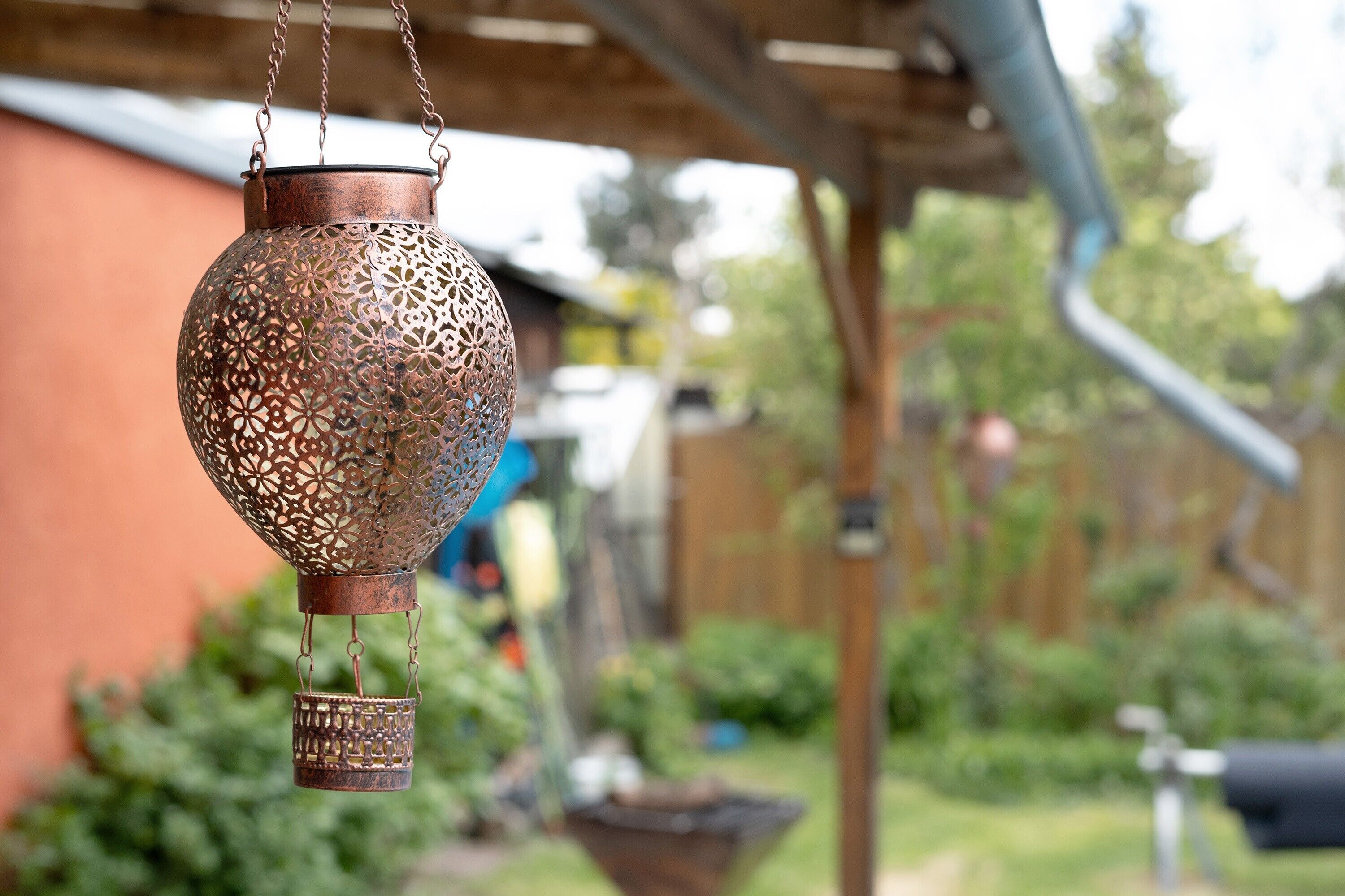 A hanging metal lantern with intricate patterns, suspended from a wooden structure.