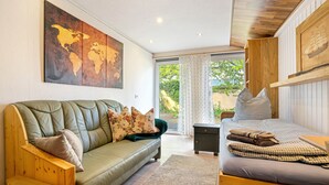 A room with a green sofa, a wooden bench, a bed with checkered bedding, a world map on the wall, and a window with curtains. - Apartment 'Ferienwohnung Mit Aufenthaltsraum' with Shared Pool, Shared Terrace and Wi-Fi (Ruhland)