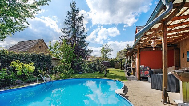 A swimming pool with a wooden deck, outdoor furniture, and a house in the background. - Apartment 'Ferienwohnung Mit Aufenthaltsraum' with Shared Pool, Shared Terrace and Wi-Fi (Ruhland)