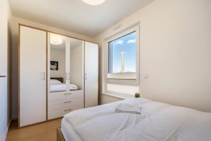 Une chambre à coucher comprenant un lit, une armoire, une fenêtre donnant sur une cheminée et une table de chevet avec une lampe.