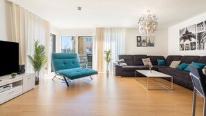 Una sala de estar moderna con un sofá, un sillón verde azulado, una mesa de centro y un televisor.