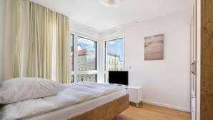 Un dormitorio con una cama de madera, un televisor, un mueble blanco pequeño y un cuadro en la pared.