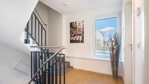 Una escalera con barandillas negras, una ventana con vista al cielo y un cuadro enmarcado en la pared.