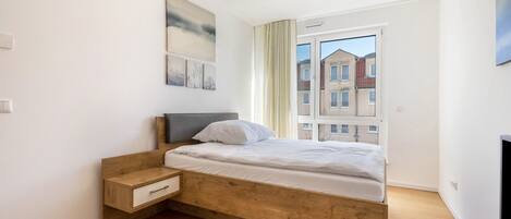 Ein Schlafzimmer mit einem hölzernen Bett, einem Nachttisch, einem Fernseher und einem Fenster mit Blick auf Gebäude.