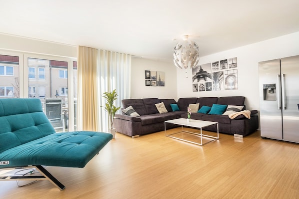 Un salon moderne avec un canapé turquoise, un canapé foncé, une table basse et un réfrigérateur.