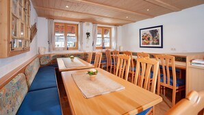 Un comedor con mesas y sillas de madera, un banco con cojines estampados y un amplio ventanal con cortinas.