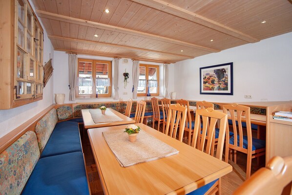 Un espace repas avec des tables et des chaises en bois, un banc agrémenté de coussins à motifs et une grande fenêtre avec des rideaux.
