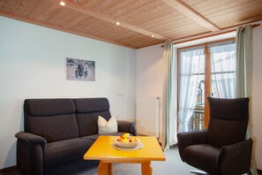 Un salon avec un canapé, un fauteuil et une table sur laquelle se trouvent des fruits.