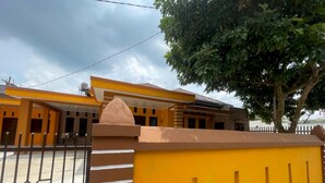 Un bâtiment jaune avec une entrée fermée par un portail, un arbre devant et un ciel dégagé.
