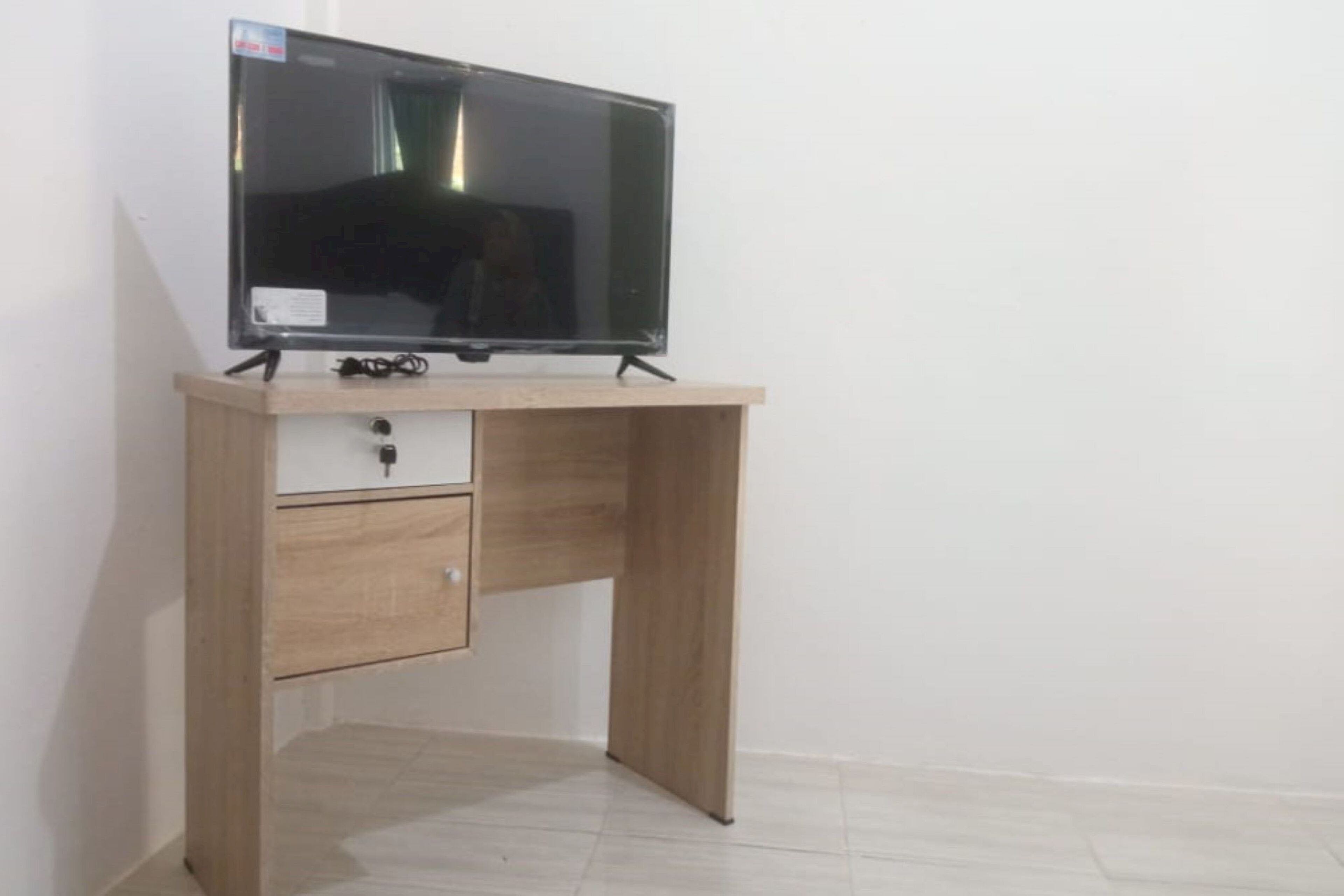 A wooden desk with a flat-screen TV, a drawer, and a cable.