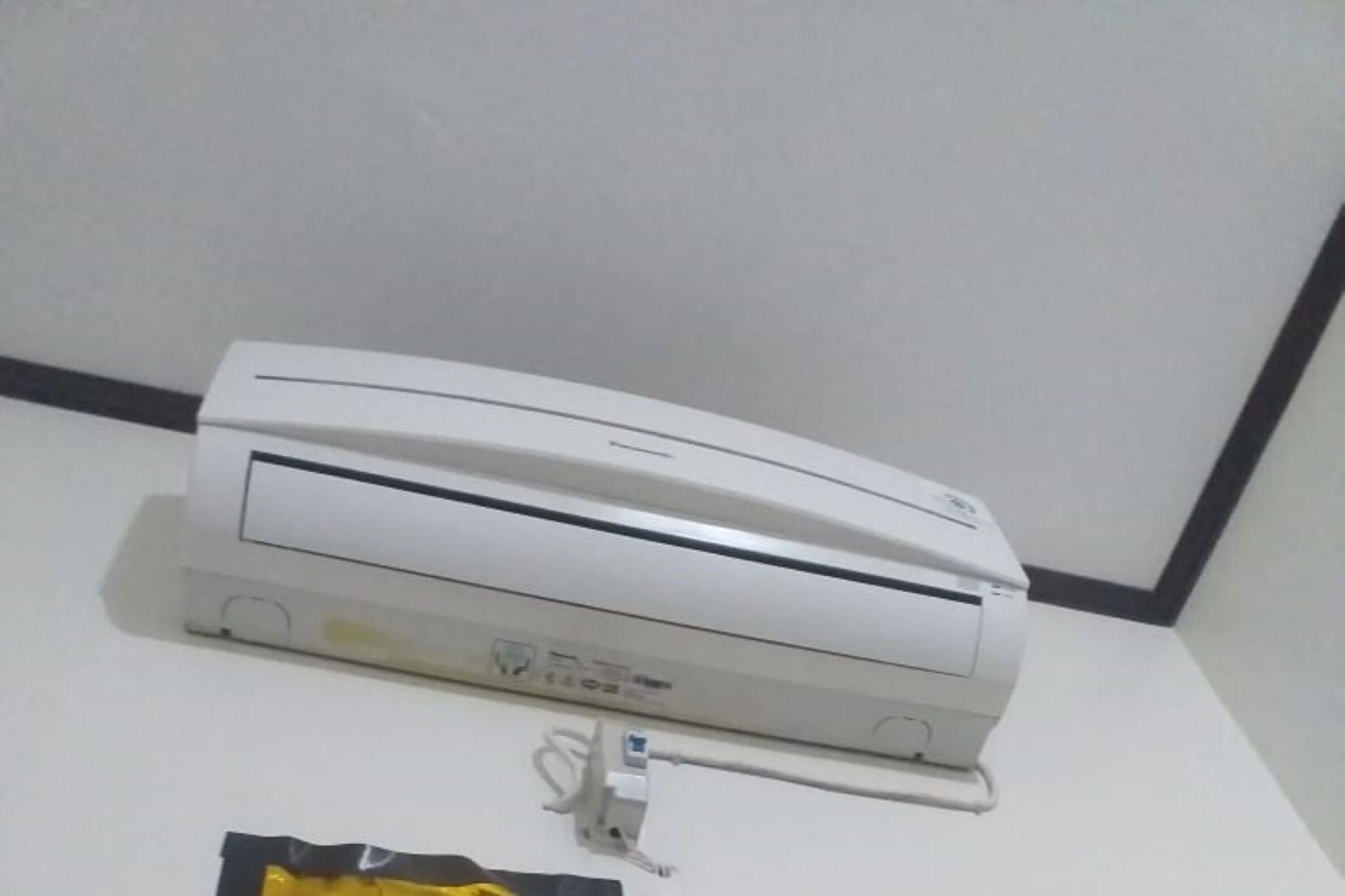 A white air conditioning unit mounted on a wall with a visible power cord.