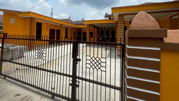 Un bâtiment jaune doté d’une cour fermée par un portail, d’un mur en briques et d’une clôture en métal.