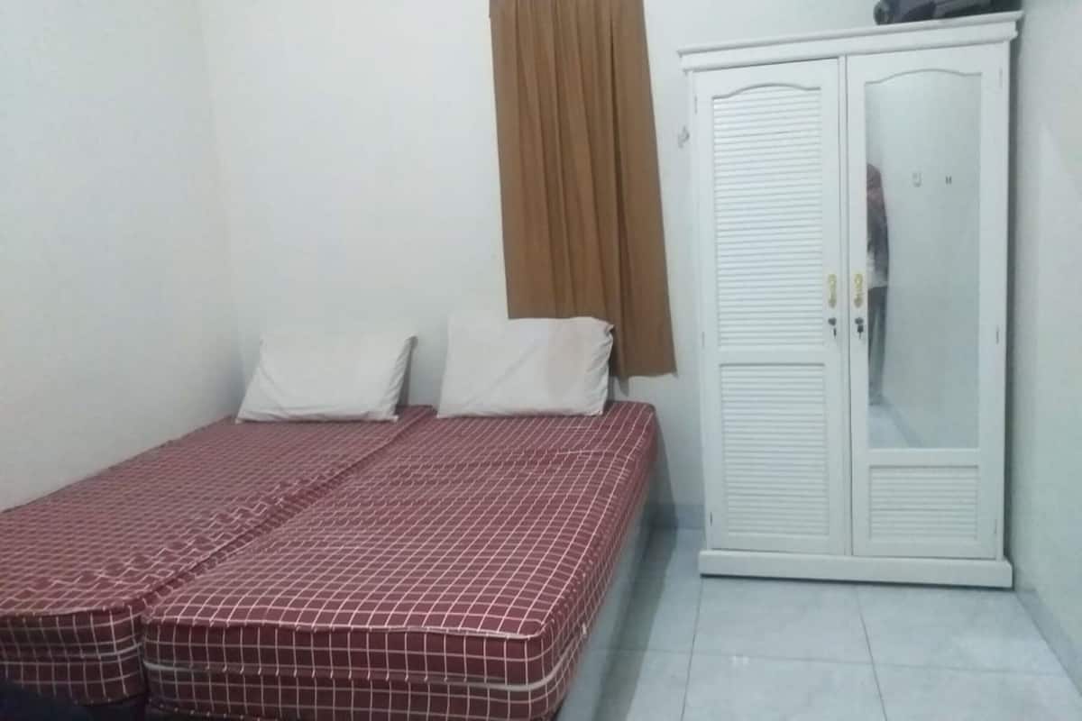 Une petite chambre avec un lit simple, un matelas à carreaux, une armoire blanche et un rideau marron.