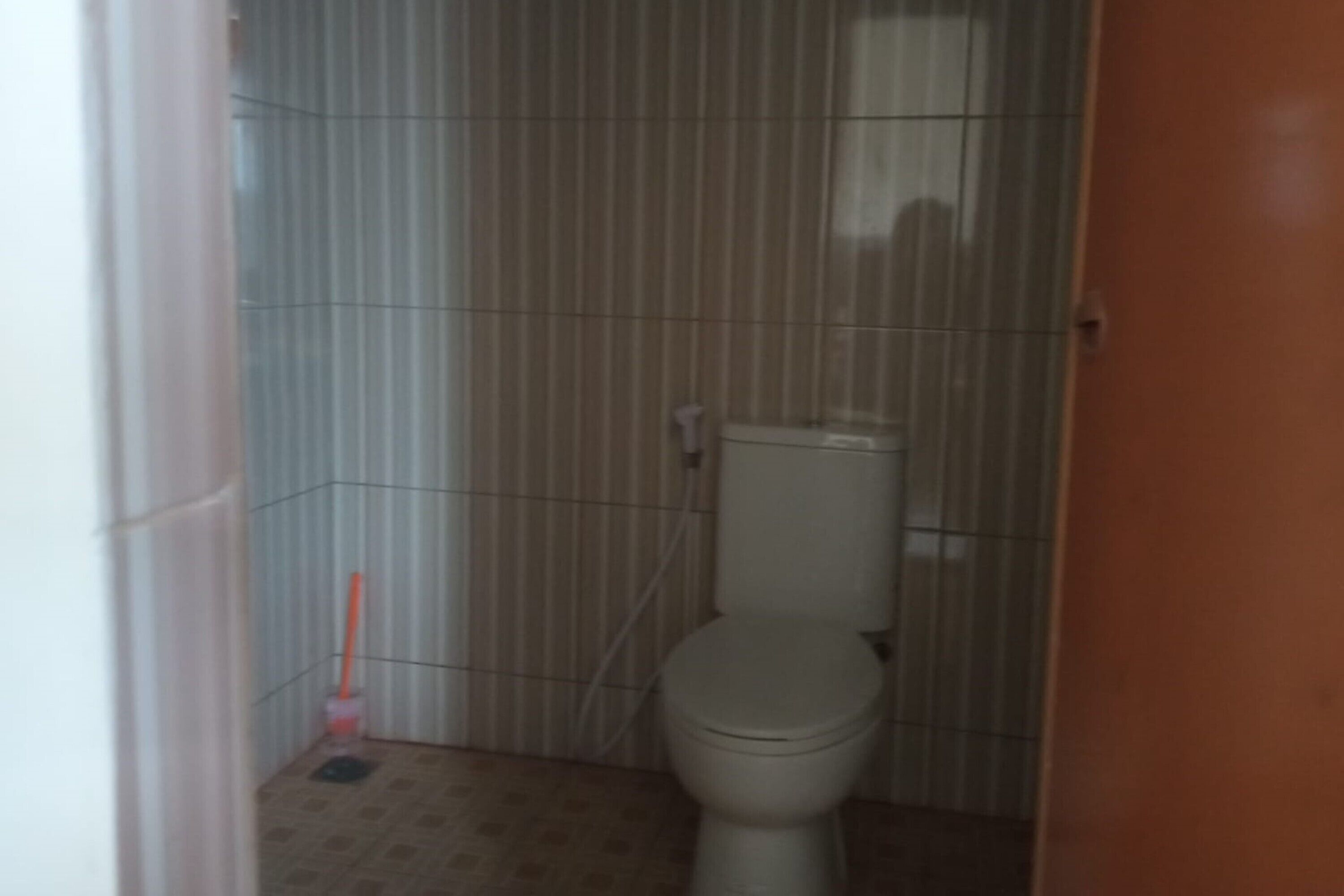 Un baño pequeño y estrecho con un inodoro, una escoba y un cubo de basura.