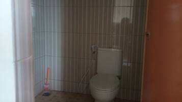 Un baño pequeño y estrecho con un inodoro, una escoba y un cubo de basura.