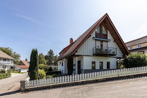 A two-story house with a balcony, a white picket fence, and a clear sky.