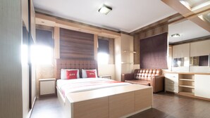 A modern bedroom with a large bed, built-in storage, a seating area, and a kitchenette. - OYO 93828 Apartemen Tamansari Panoramic By Narel Room (Bandung)