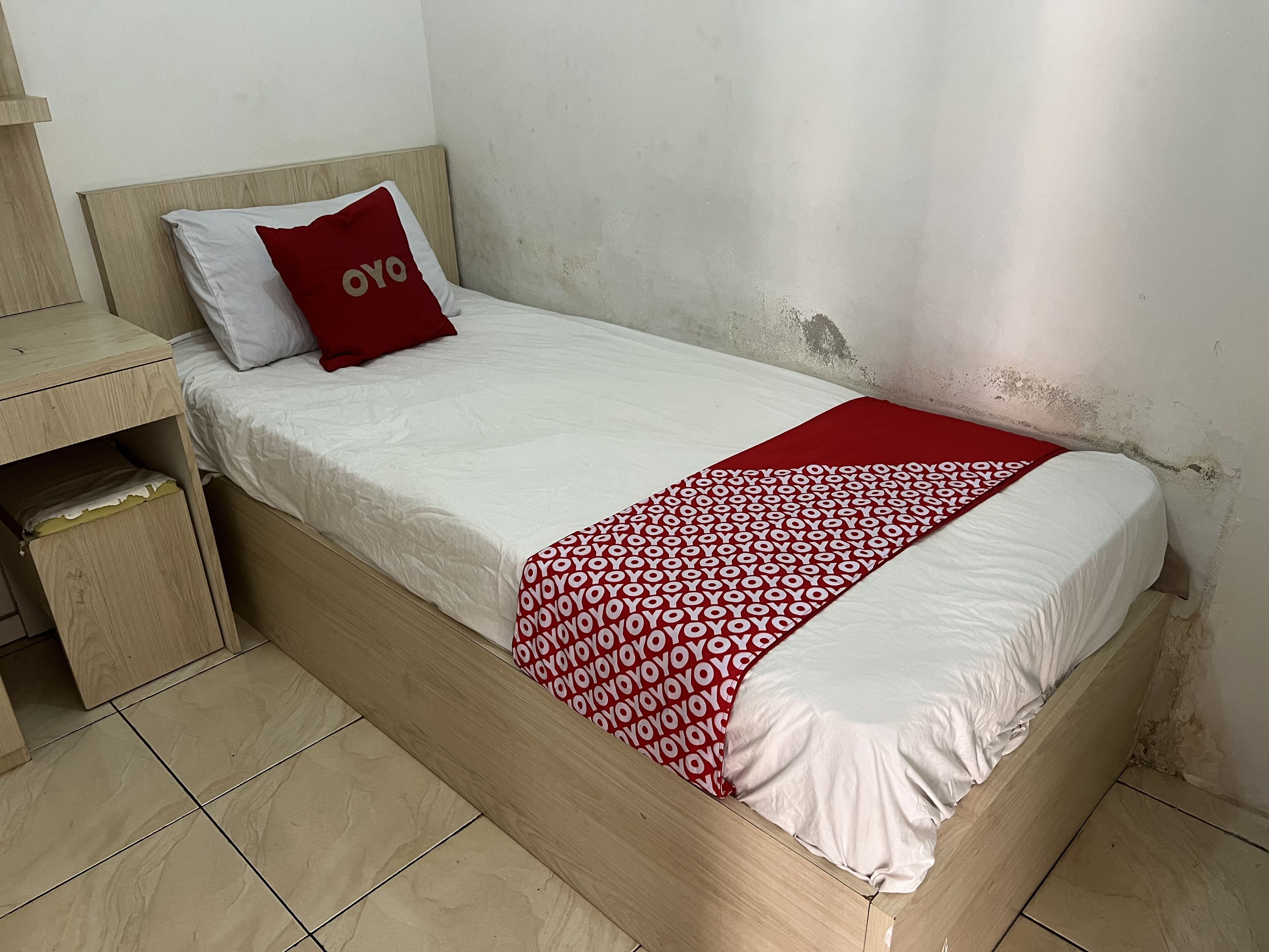 Un lit simple avec un matelas blanc, un oreiller rouge et une couverture rouge à motifs.