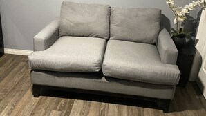 A grey sofa in a room with wooden flooring and a grey wall. - Cozy Get-Away Suite (Regina)