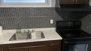 A kitchen with a double sink, a black stove, and a microwave. - Cozy Get-Away Suite (Regina)
