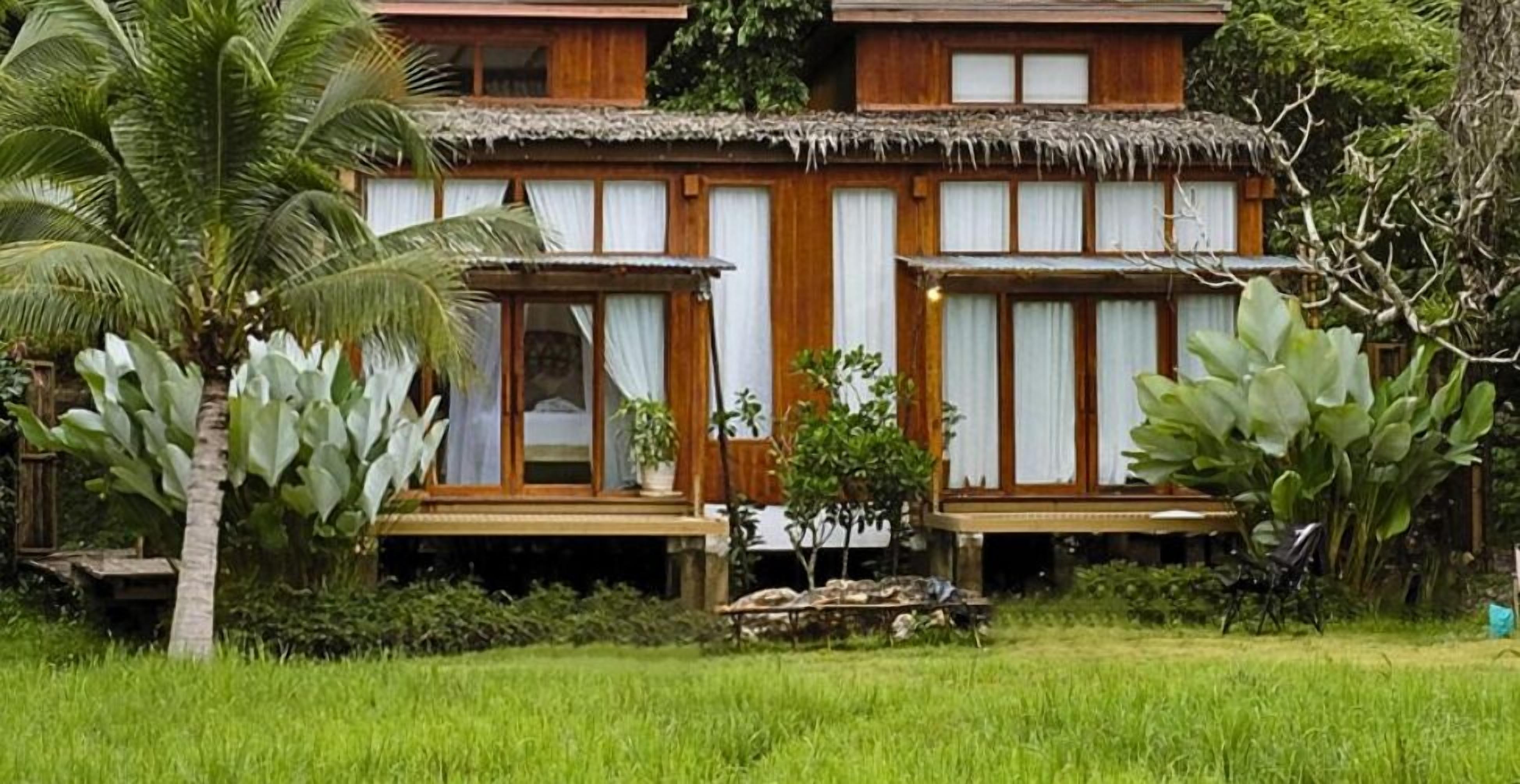 Un alojamiento tipo cabaña con techo de paja, fachada de madera y un exuberante jardín.