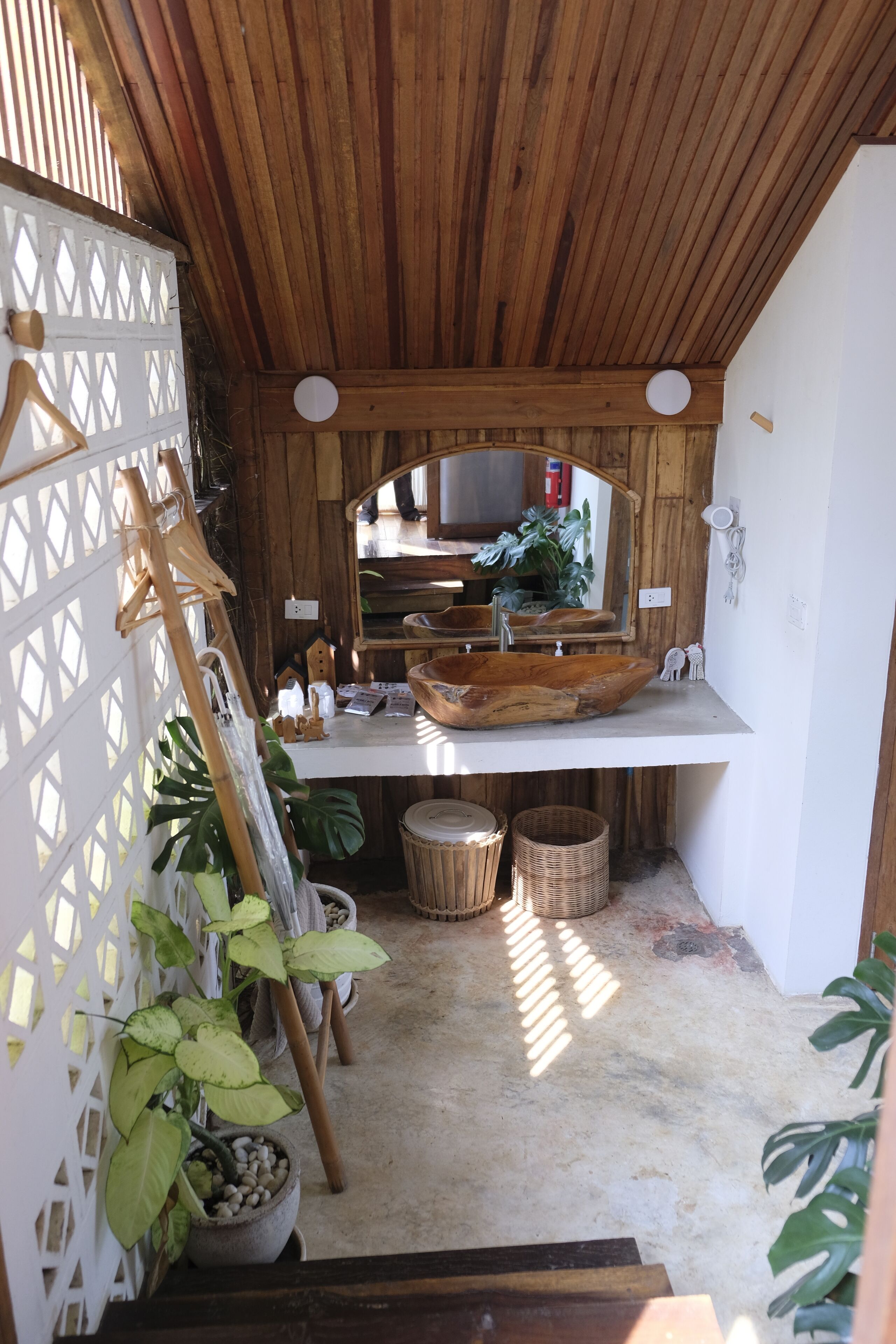 A rustic bathroom with a wooden ceiling, a large mirror, a wooden basin sink, and potted plants.