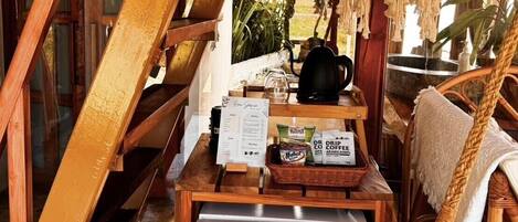 Une pièce chaleureuse avec un escalier en bois, un luminaire suspendu en macramé, un coin café avec un mini-réfrigérateur et des meubles en osier.