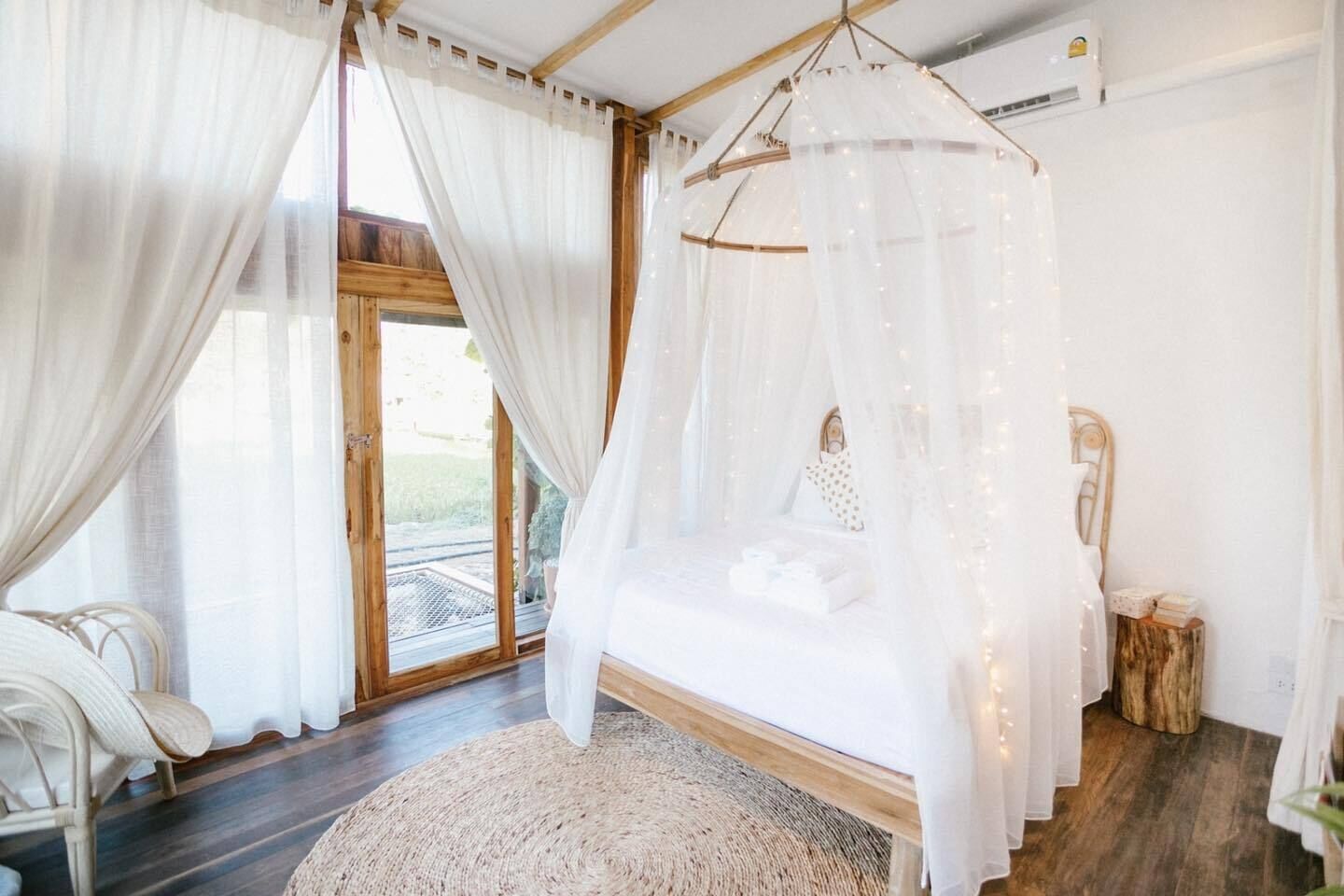Ein Schlafzimmer mit Baldachinbett, einem Korbstuhl, einem Holztischchen und Blick ins Freie.