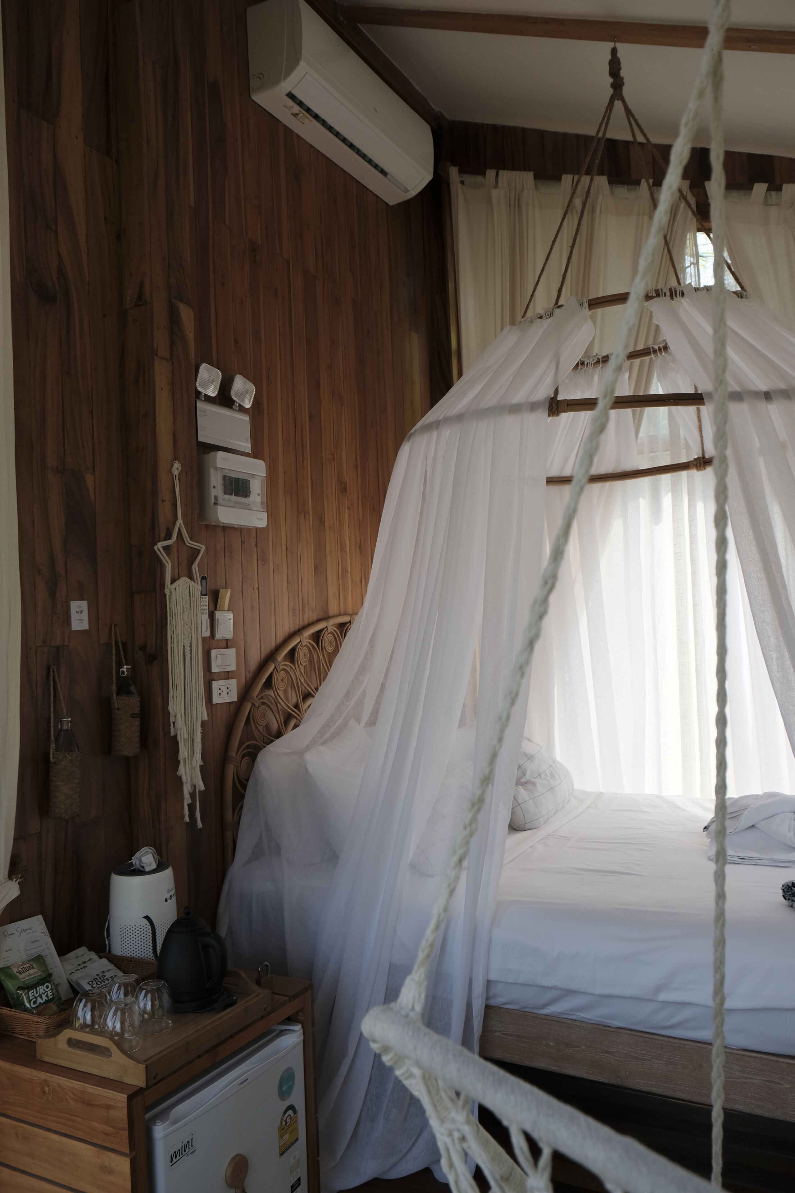A bedroom with a wooden floor, a bed with a canopy, a bedside table with a kettle, and a dresser.