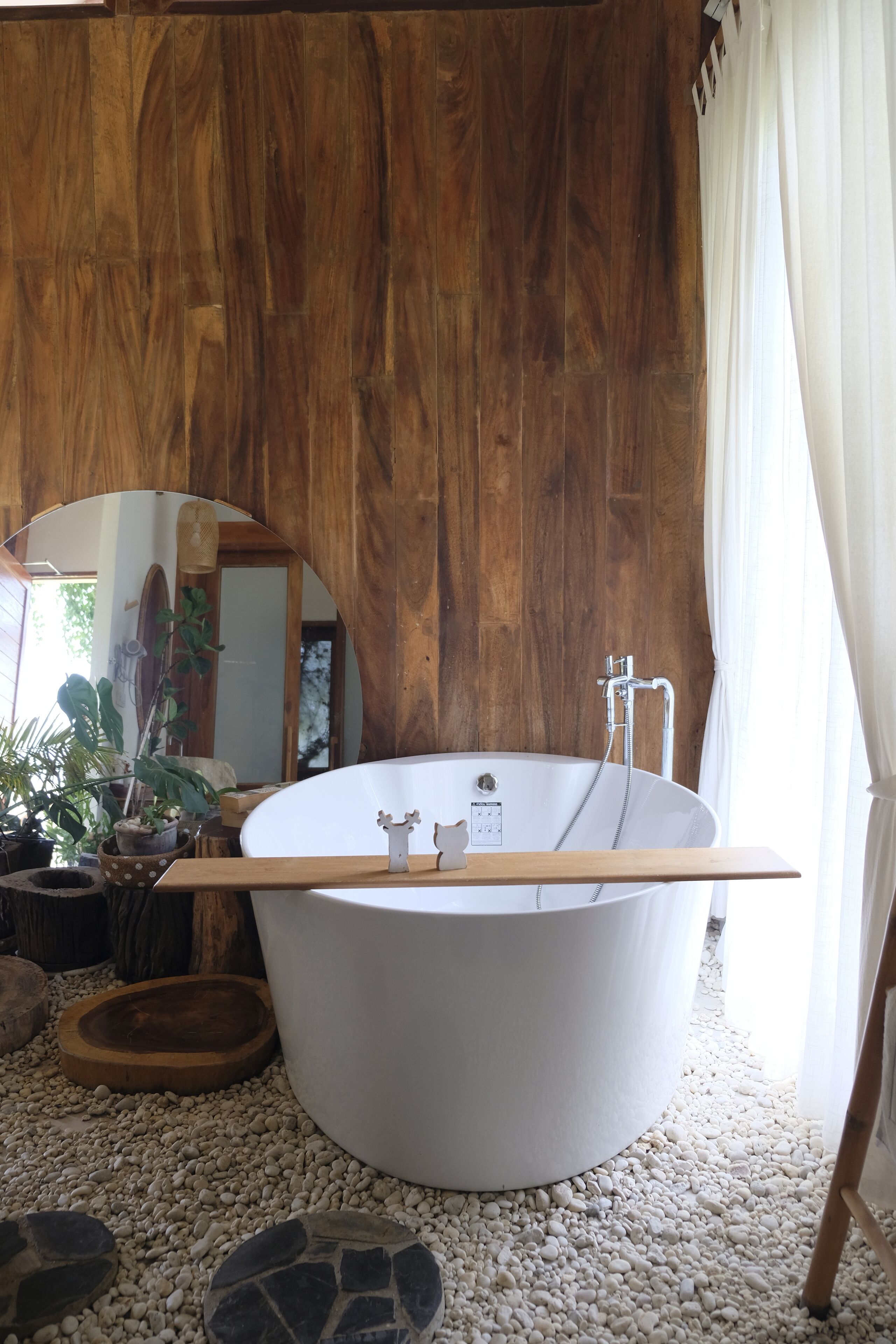 Un baño moderno con una bañera independiente, suelo de madera y un espejo que refleja la habitación.