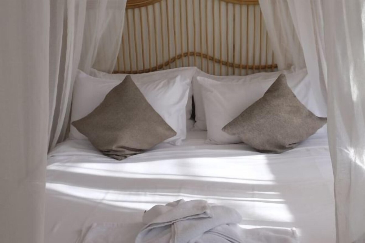 Una cama con dosel, almohadas y manta.