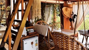 Un interior rústico de madera con una silla colgante, una cesta de mimbre y un refrigerador pequeño.