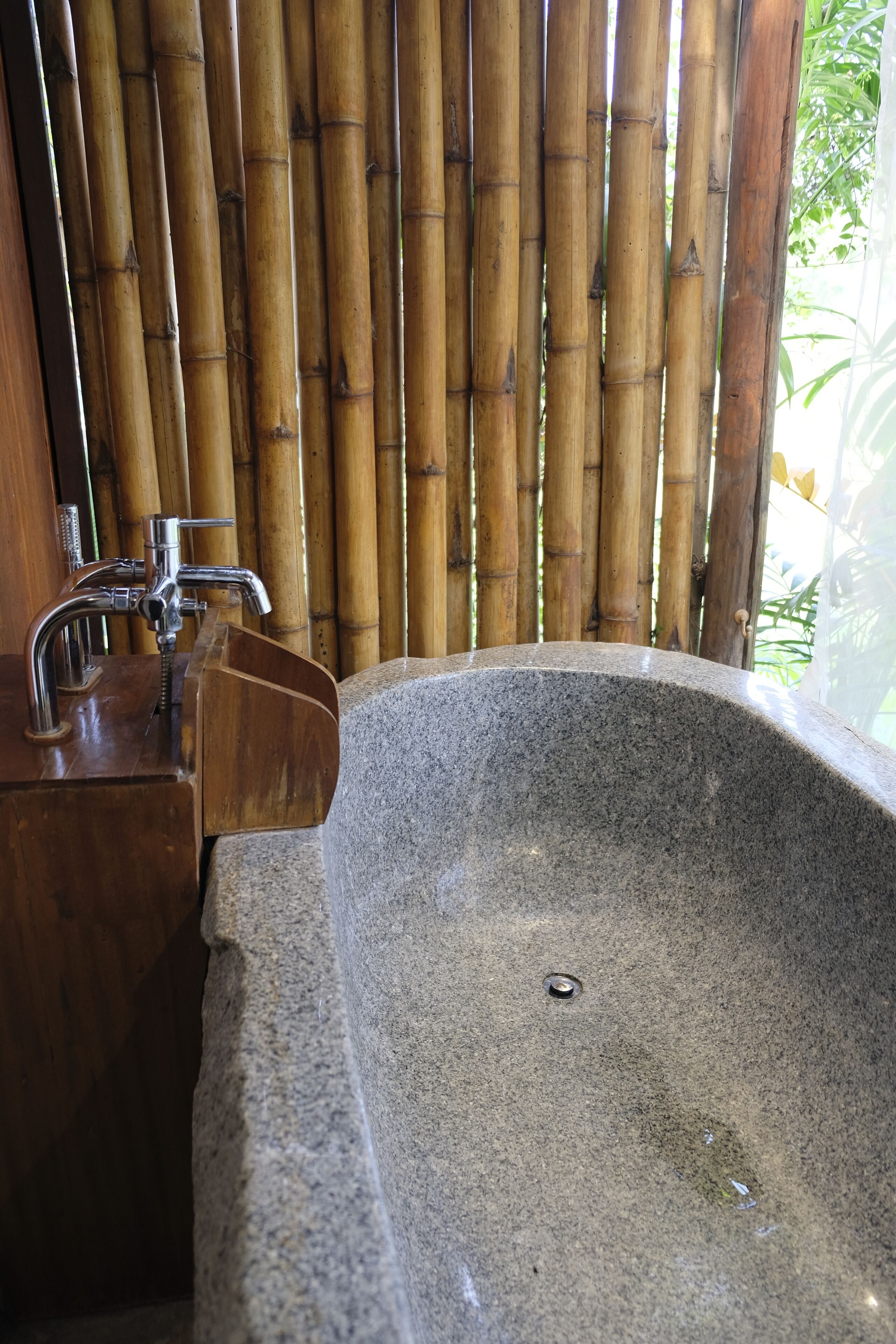 A stone sink with a faucet and a wooden cabinet, set against a bamboo backdrop.