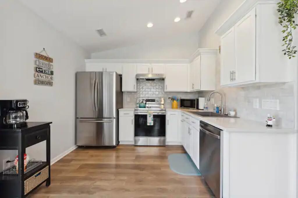 A modern kitchen with white cabinets, stainless steel appliances, and a wooden floor.
