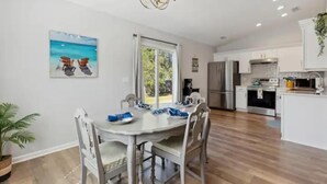A modern kitchen with white cabinets, stainless steel appliances, and a dining area with a white table and chairs. - Beach House Vacation  (Wilmington)