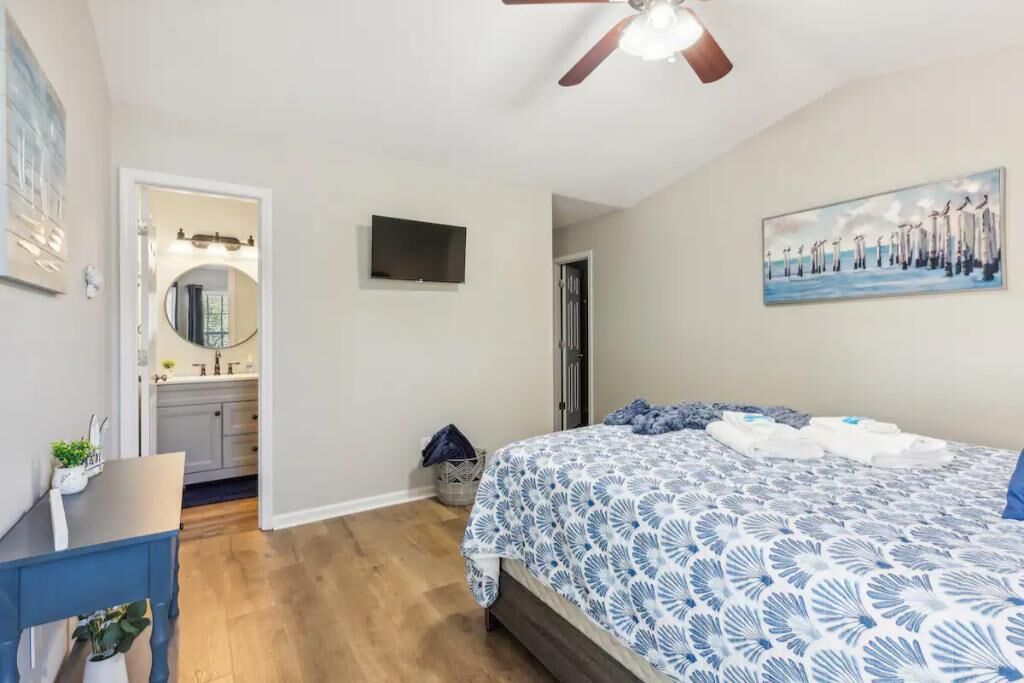 A bedroom with a bed, a ceiling fan, a TV, and a painting on the wall.