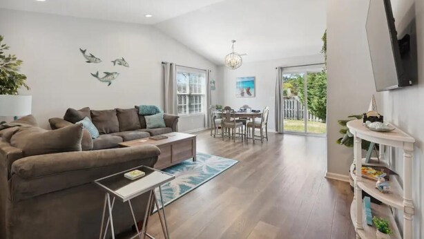 A modern living room with a brown sofa, a coffee table, and a dining area with a chandelier. - Beach House Vacation  (Wilmington)