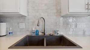 A kitchen with a double sink, white cabinets, and a tiled backsplash. - Beach House Vacation  (Wilmington)