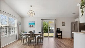 A spacious kitchen with a dining area, wooden flooring, a chandelier, and a sliding glass door leading to a backyard. - Beach House Vacation  (Wilmington)